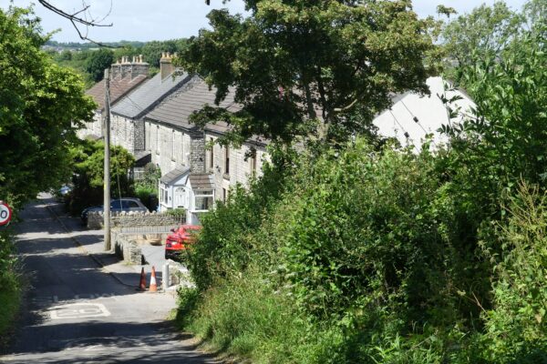 Radstock Town Council to Showcase Neighbourhood Plan Progress at Annual Town Meeting Image shows a quiet road road. with houses on the right hand side, and green hedges and trees beside and opposite.