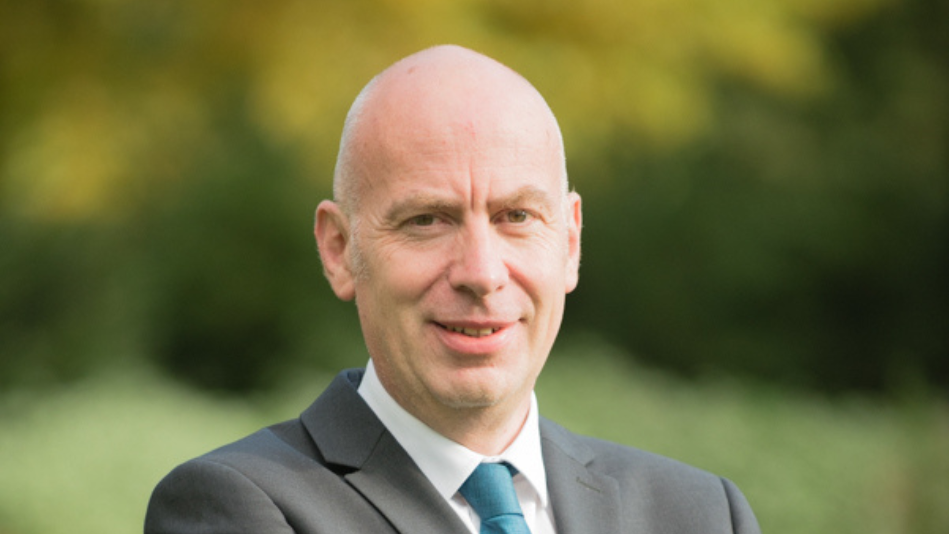 Image shows a man wearing a suit and blue tie.